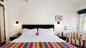 Habitación de hotel con una cama grande, dos mesitas de noche, una silla, un ventilador de techo y una puerta con ventana.