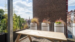Una terraza en la azotea con una mesa de madera y macetas con plantas.