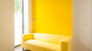 Una habitación con un sofá amarillo frente a una pared amarilla, una ventana y una puerta.