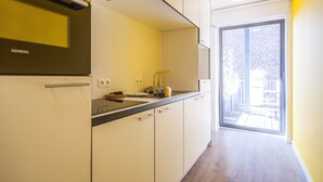 Una cocina moderna con armarios blancos, una encimera negra y un refrigerador Siemens. Se ve una ventana con vistas a un edificio de ladrillo.