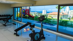 A gym with exercise equipment and large windows overlooking a playground and cityscape. - Water Park Condominium by Able Estate (Pattaya)