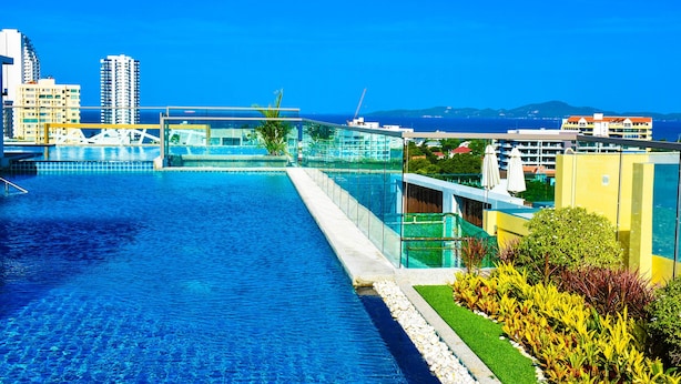 A swimming pool with clear blue water, surrounded by buildings and a view of the sea. - Water Park Condominium by Able Estate (Pattaya)