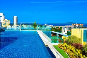 A swimming pool with clear blue water, surrounded by buildings and a view of the sea.