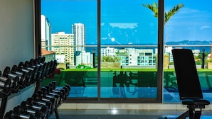 A gym with exercise equipment and a large window offering a city view. - Water Park Condominium by Able Estate (Pattaya)