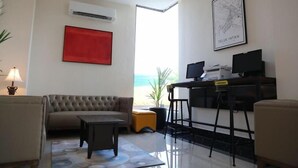 A modern living room with a sofa, a coffee table, a desk with two monitors, and a red artwork on the wall. - Rivertel (Teluk Intan)