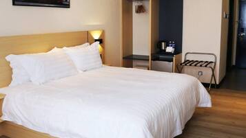 Una habitación de hotel con una cama grande, un armario, un escritorio con una silla y un perchero.