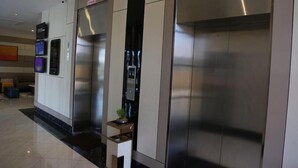 A modern elevator area with stainless steel elevators, a small table with a plant, and digital displays on the wall. - Rivertel (Teluk Intan)