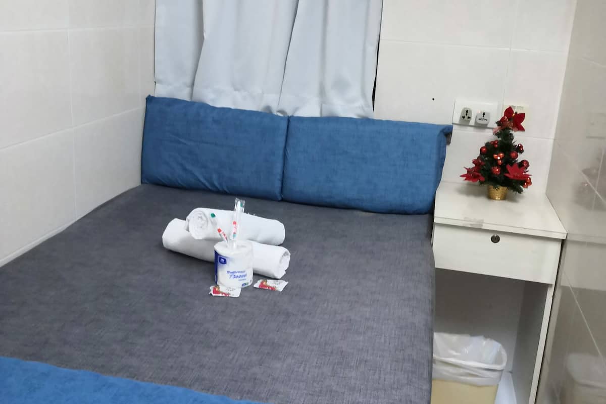 A hotel room with a bed, a small table with toiletries, a nightstand, and a decorative plant.