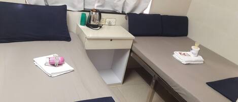 A small, neatly arranged room with two beds, a desk, and a window with curtains.