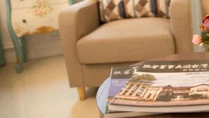 A beige armchair with a patterned pillow, a small side table with a floral design, and a magazine on a wooden surface. - Canova (Ji'an)