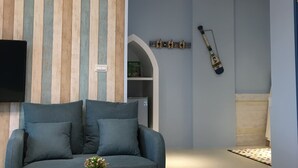 A living room with a sofa, a coffee table, a TV mounted on the wall, and a decorative wall panel. - Canova (Ji'an)