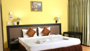 A hotel room with a bed, two nightstands, a lamp, a painting, and a curtain. - Alor Grande Holiday Resort (Candolim)