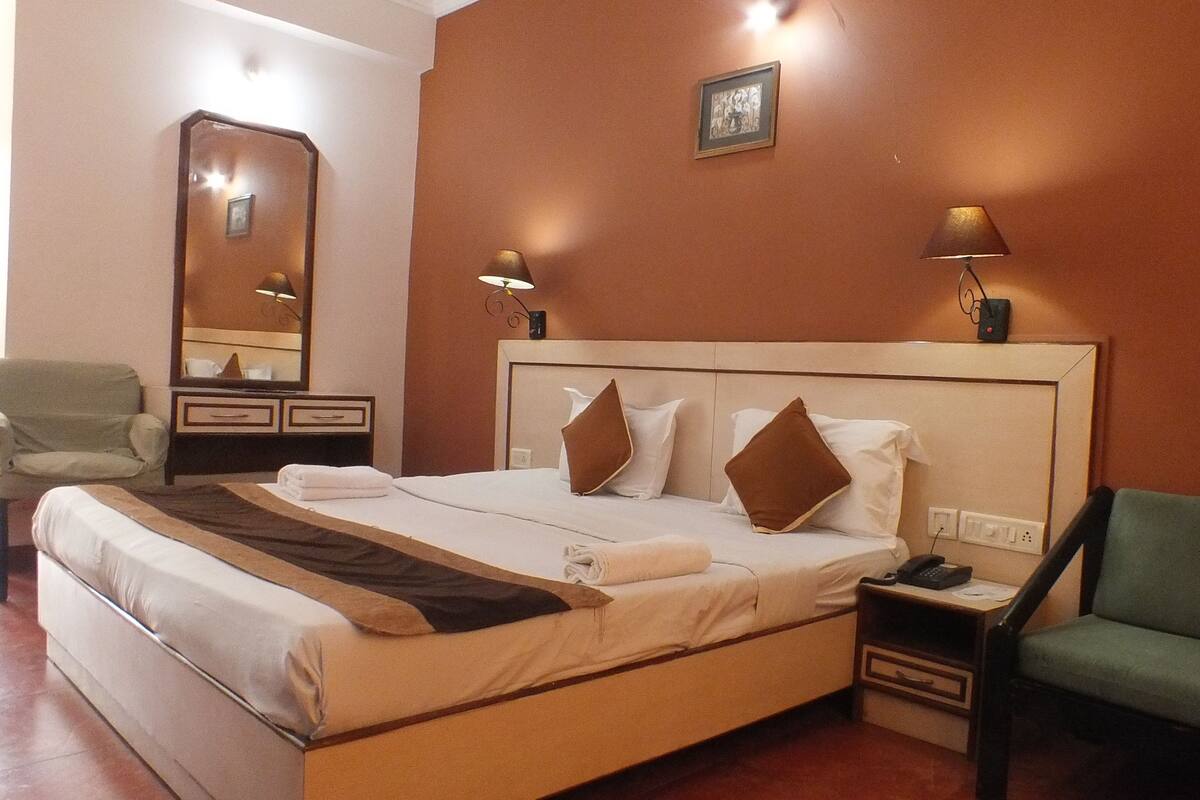 A hotel room with a large bed, two bedside lamps, a chair, a desk with a phone, and a mirror.