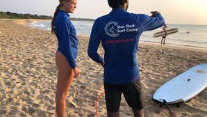 A beach scene with two people wearing blue shirts, one labeled "SURF INSTRUCTOR".