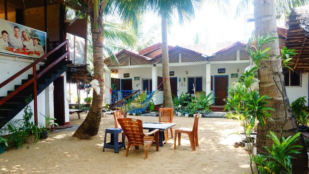 A beachside building with a staircase, outdoor seating, and palm trees.