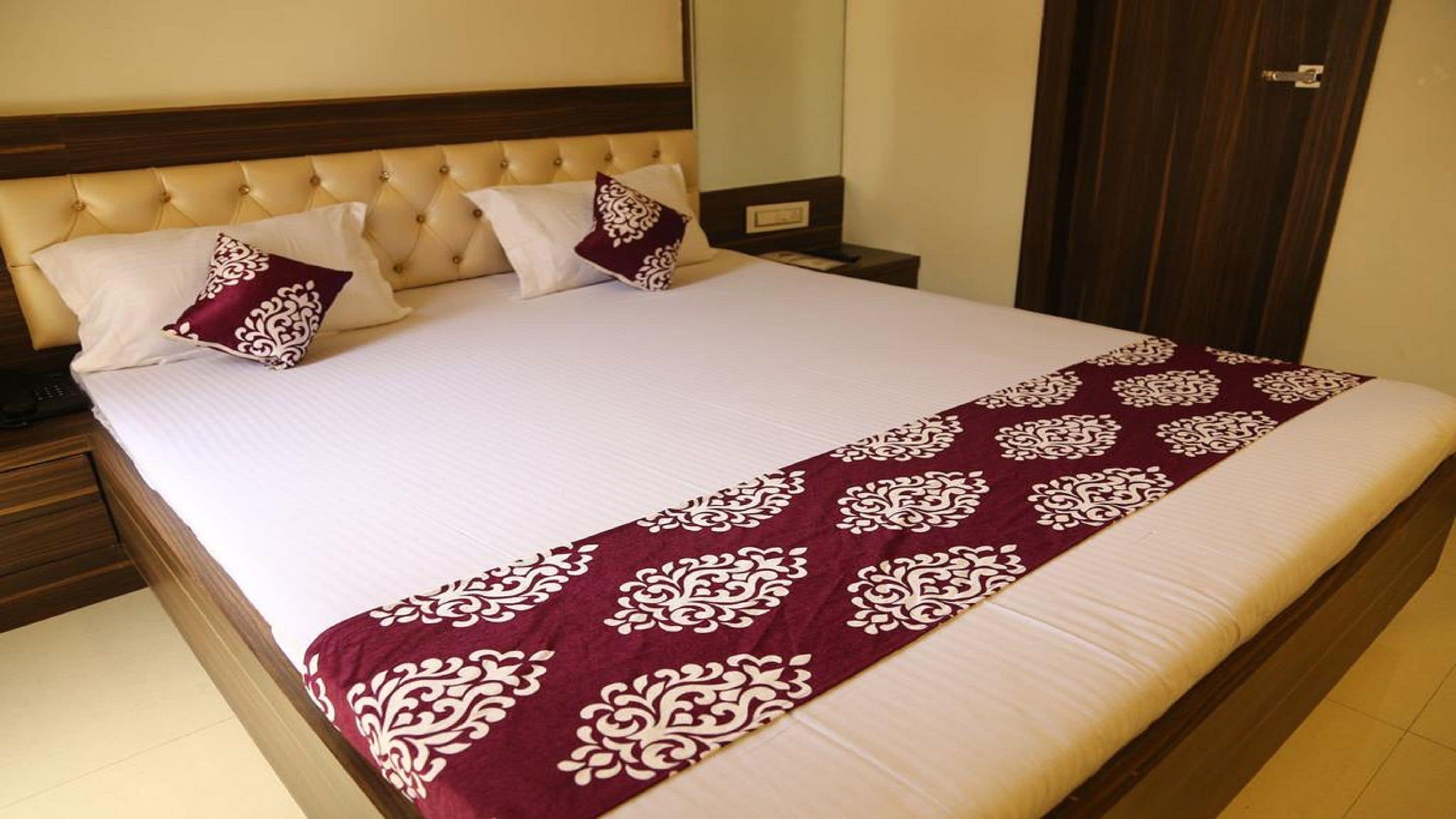A neatly made bed with a white and maroon bedspread, a matching throw, and two decorative pillows.