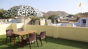 Una terraza en la azotea con una mesa, sillas, un paraguas estampado y una bandera.