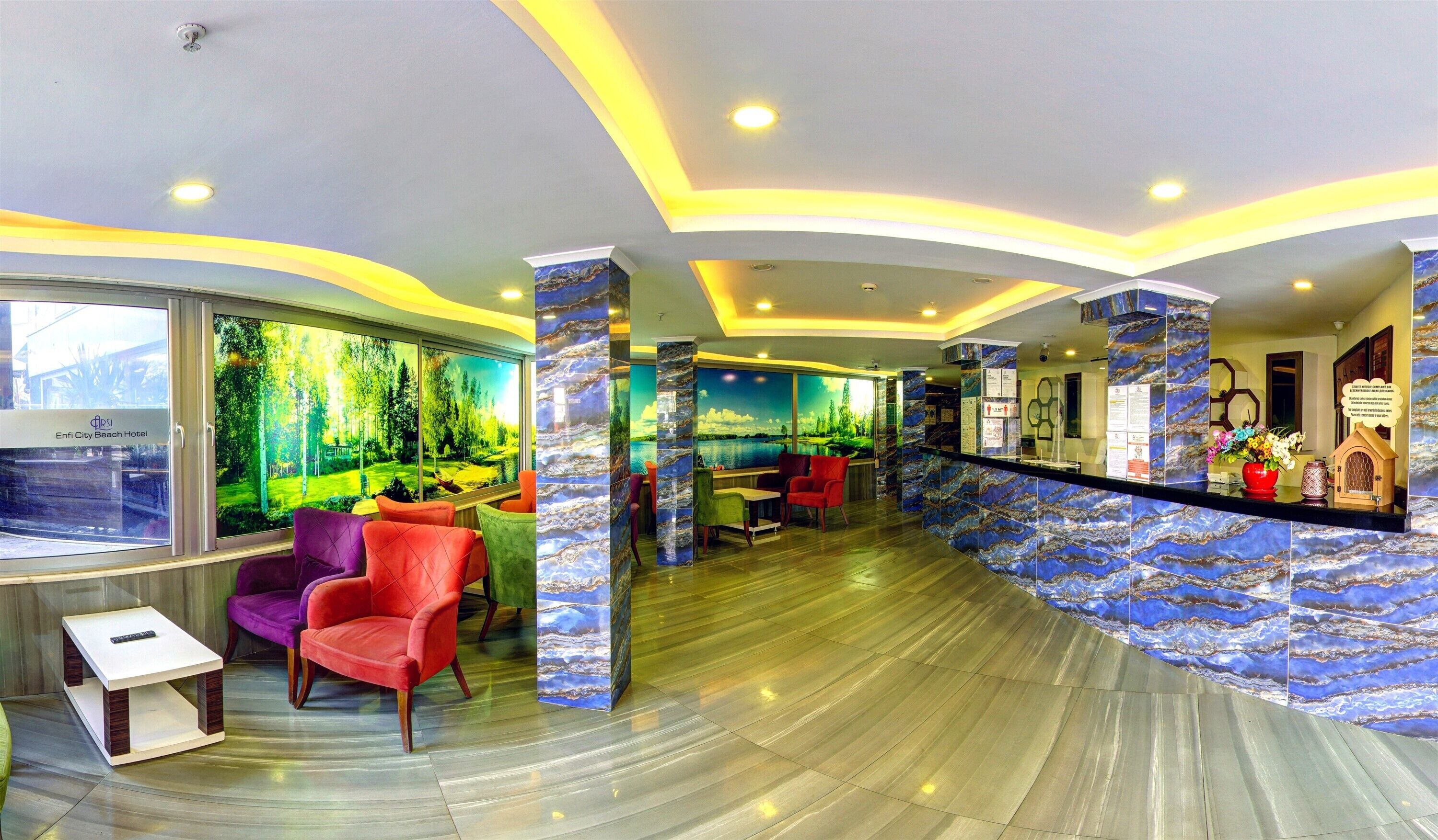 A hotel lobby with a reception desk, colorful chairs, a large window with a forest view, and a marble wall.