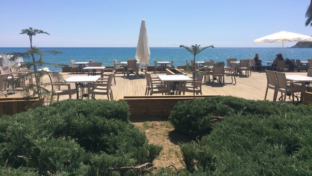 An outdoor seating area with tables and chairs facing the sea, surrounded by greenery. - Arsi Enfi City Beach Hotel (Alanya)