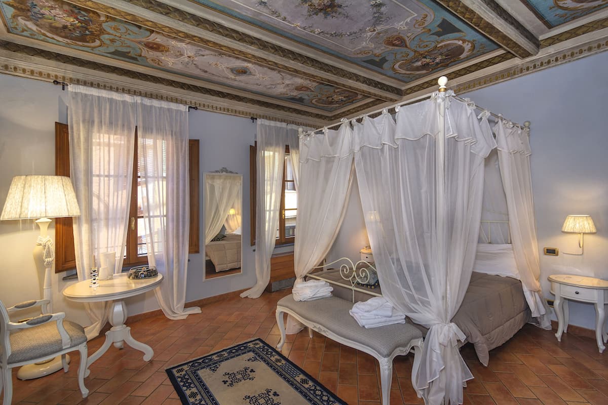 A bedroom with a four-poster bed, a sitting area with a table and chair, and a mirror.