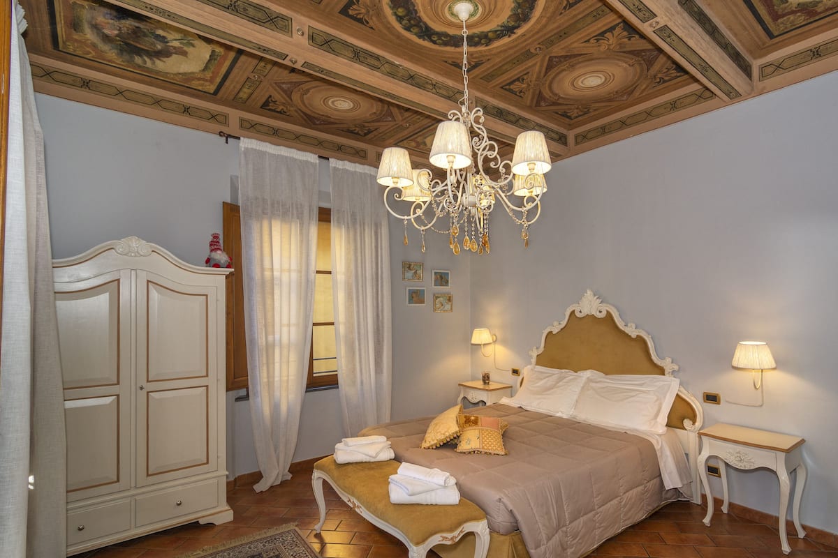 A bedroom with a large bed, a wardrobe, a chandelier, and a nightstand.