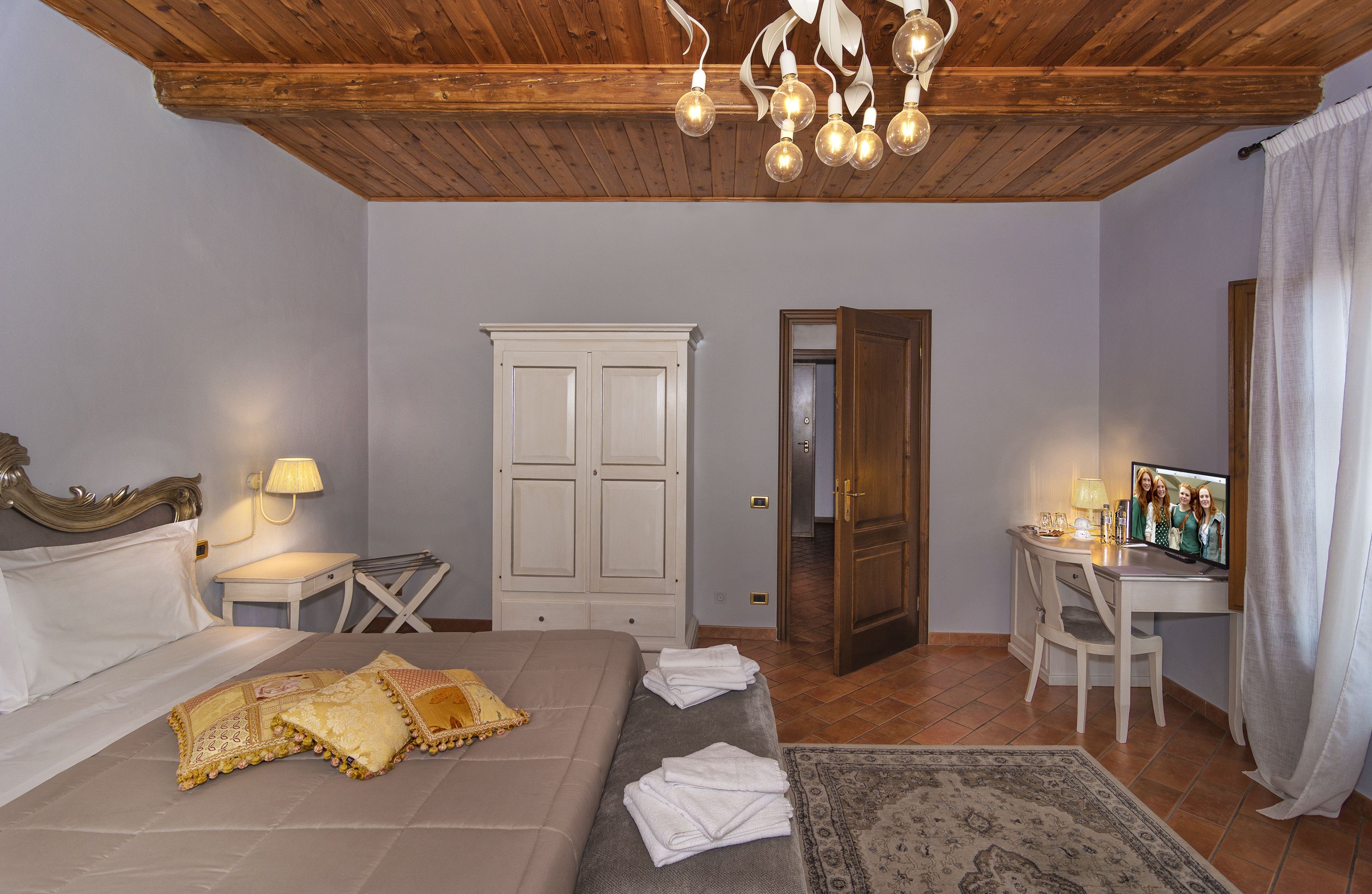 A bedroom with a bed, bedside tables, a desk, a chair, a wardrobe, and a television.