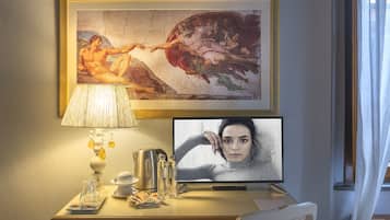 A hotel room with a desk, a framed painting, a television, and a lamp.