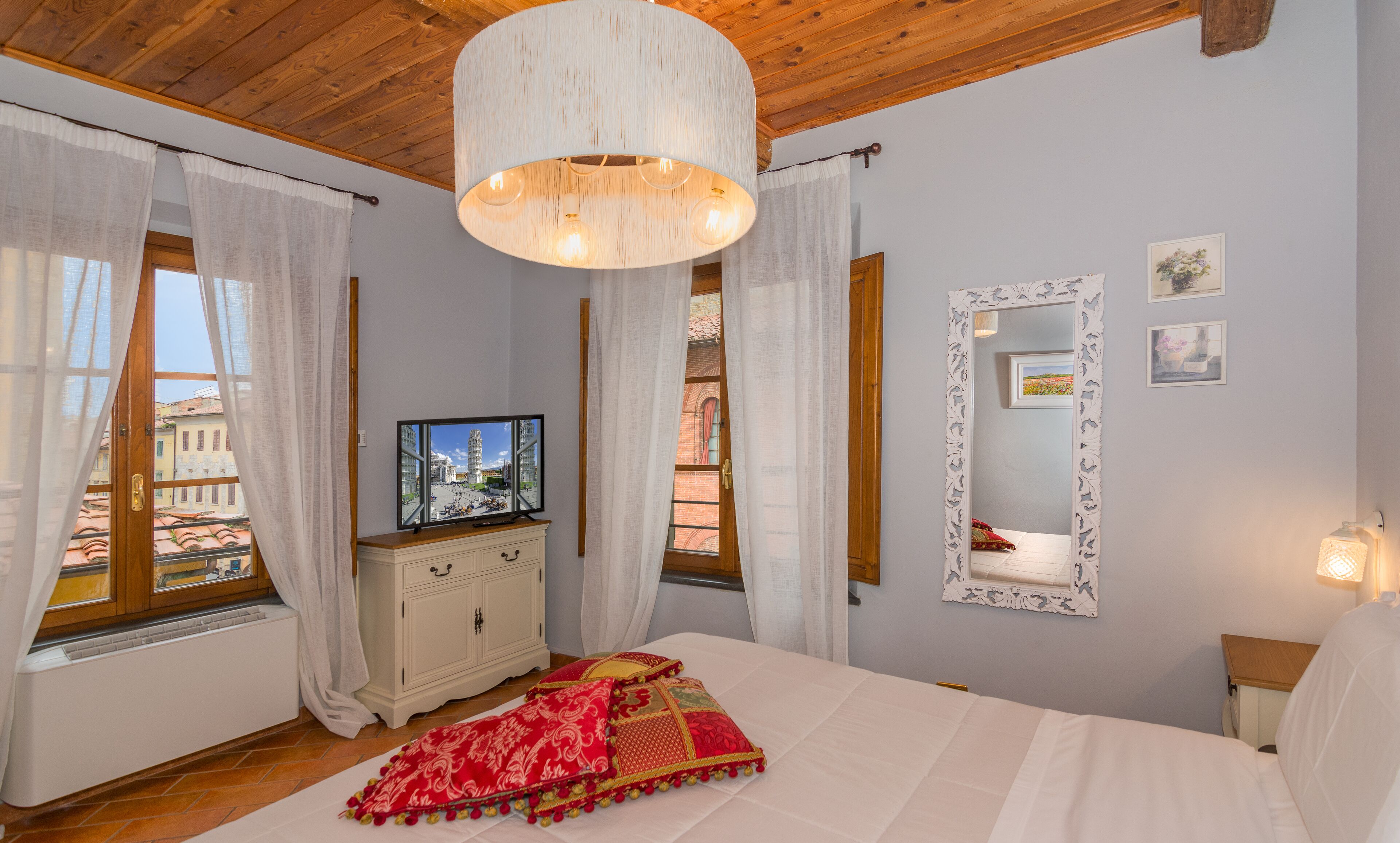 A bedroom with a bed, a television, a dresser, and a window with curtains.