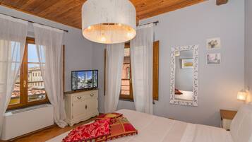 A bedroom with a bed, a television, a dresser, and a window with curtains.
