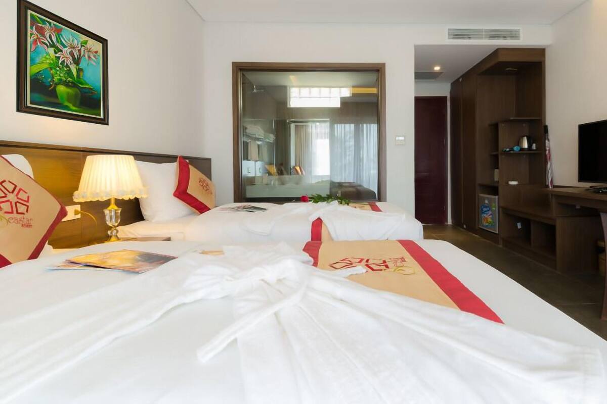 A hotel room with two beds, a desk, a TV, and a large mirror.