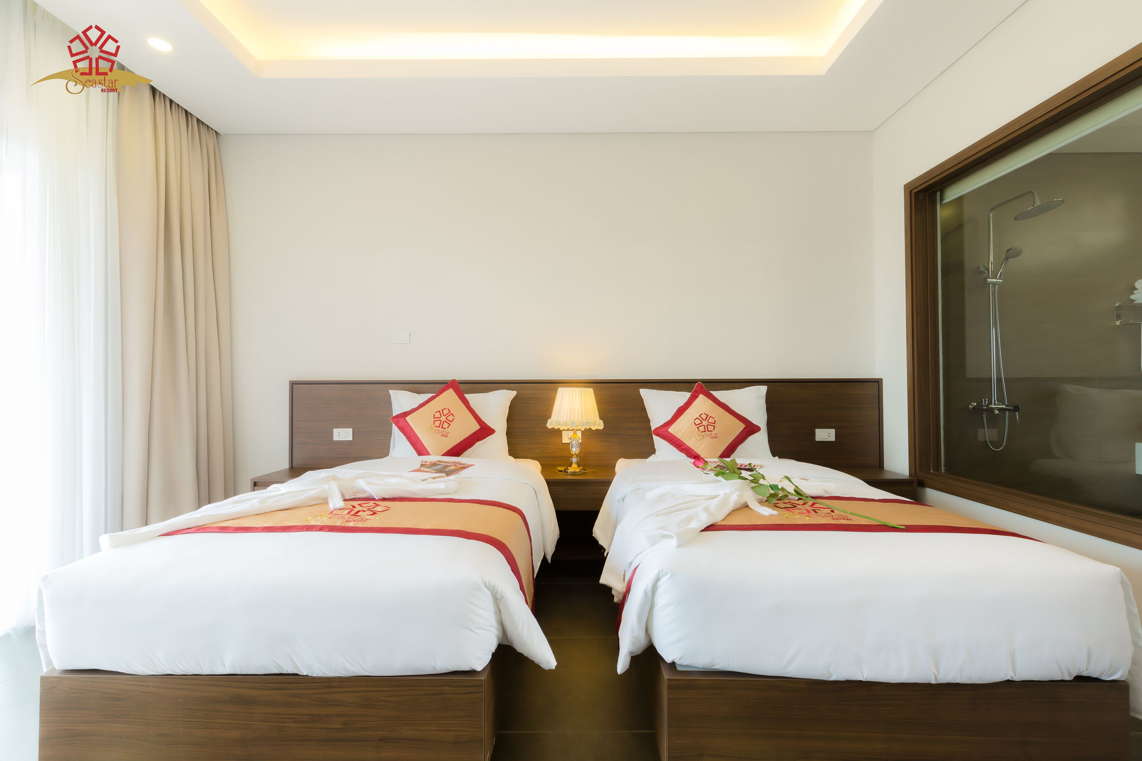 Une chambre d’hôtel avec deux lits, une table de chevet avec une lampe, un espace douche et une vue sur l’extérieur.
