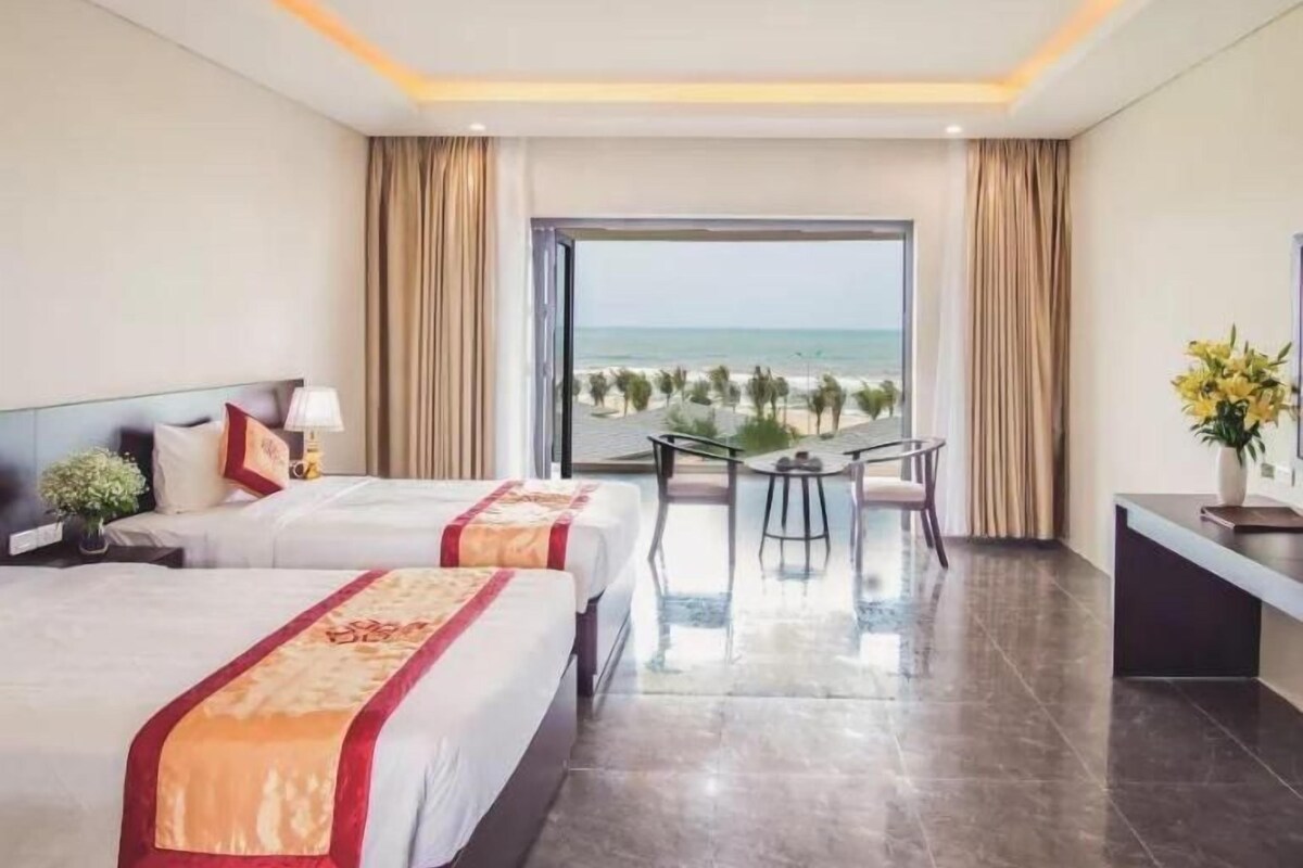 Habitación de hotel con dos camas, una mesa de comedor, sillas y vista al océano.