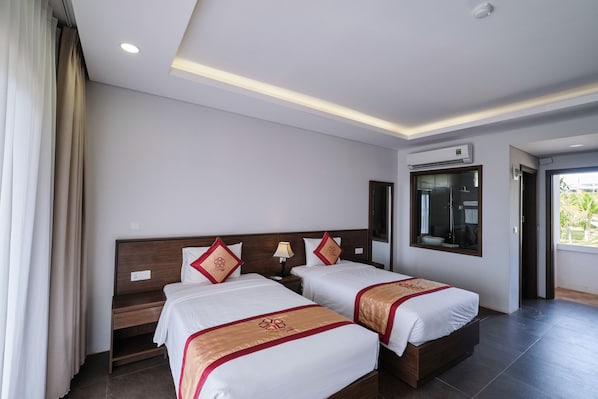 Une chambre d’hôtel avec deux lits, un bureau, une lampe, un appareil de climatisation et une fenêtre donnant sur un paysage agréable.
