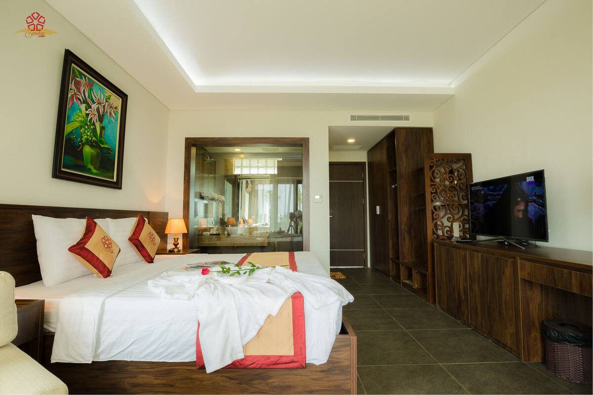 A hotel room with a large bed, a TV, a mirror, and a wooden cabinet.