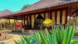 A traditional wooden structure with a tiled roof, surrounded by tropical plants and palm trees.
