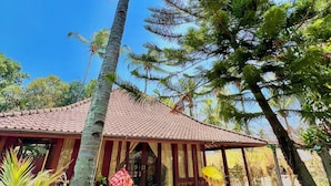 A traditional house with a tiled roof, surrounded by palm trees and tropical plants.