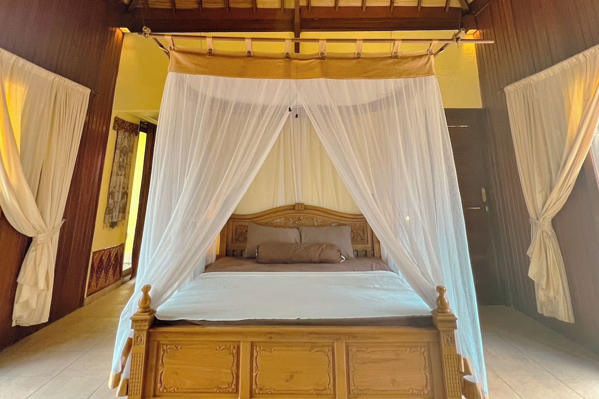 A spacious bedroom with a wooden four-poster bed, a ceiling fan, and a large window.