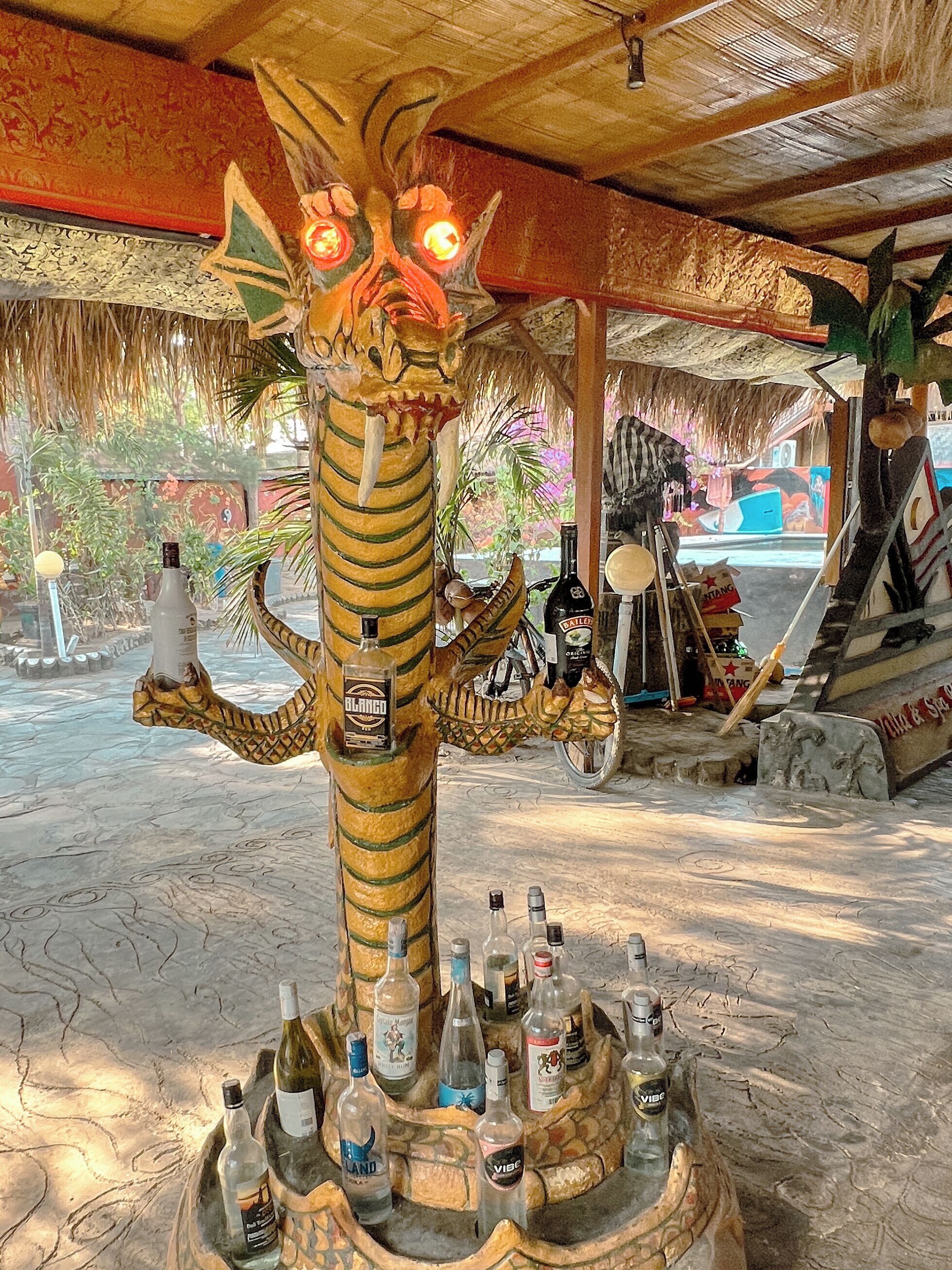 Un bar tiki con un'imponente statua di drago decorata, che sorregge bottiglie di alcolici.