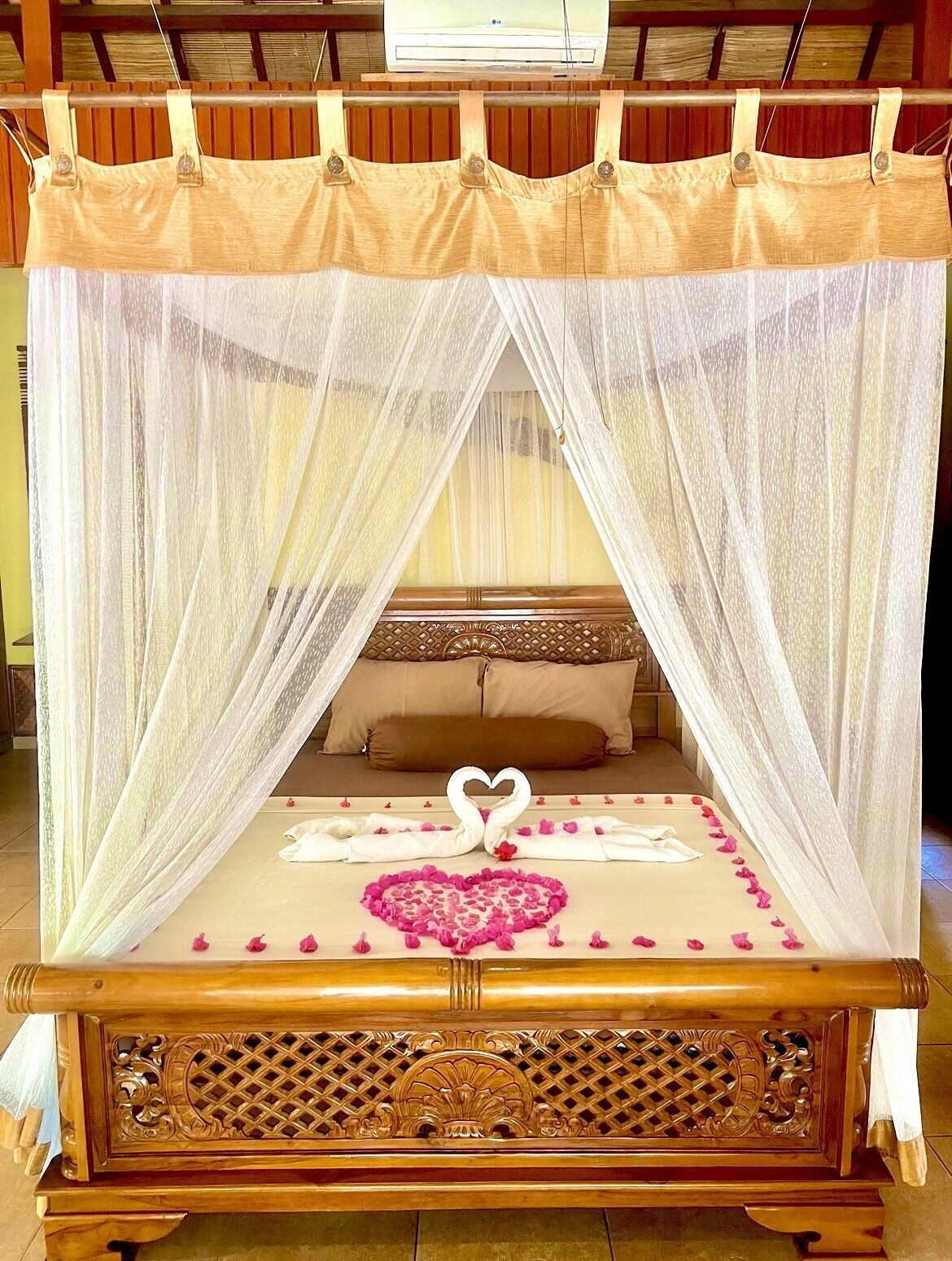 Un letto a baldacchino con tende, un composizione a forma di cuore di petali di rosa e una decorazione a forma di cigno sul letto.