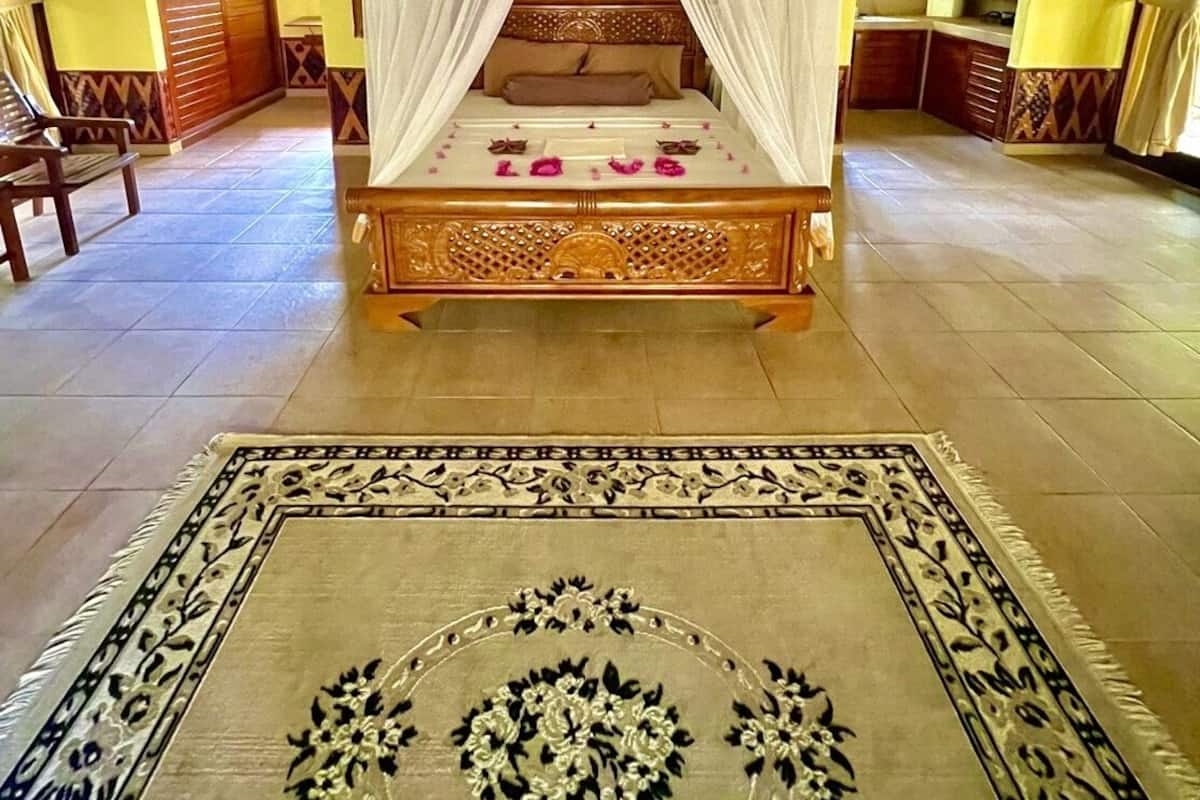 A room with a four-poster bed, a large ornate rug, and a ceiling fan.