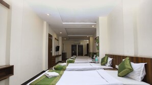 A hotel room with multiple beds aligned in a row, each with white bedding and green headboards. - Treebo Ashoka Palace Ujjain (Ujjain)