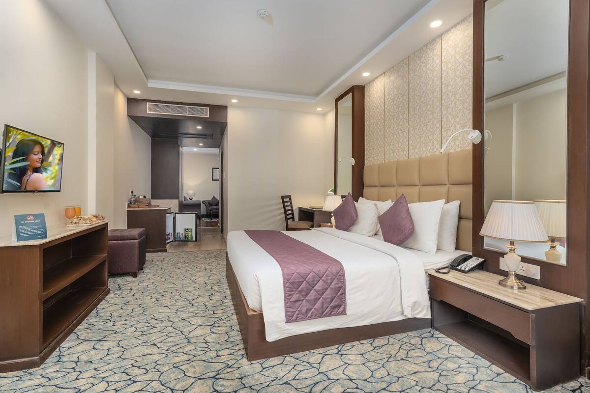 A hotel room with a bed, bedside table, lamp, and a TV on the wall.