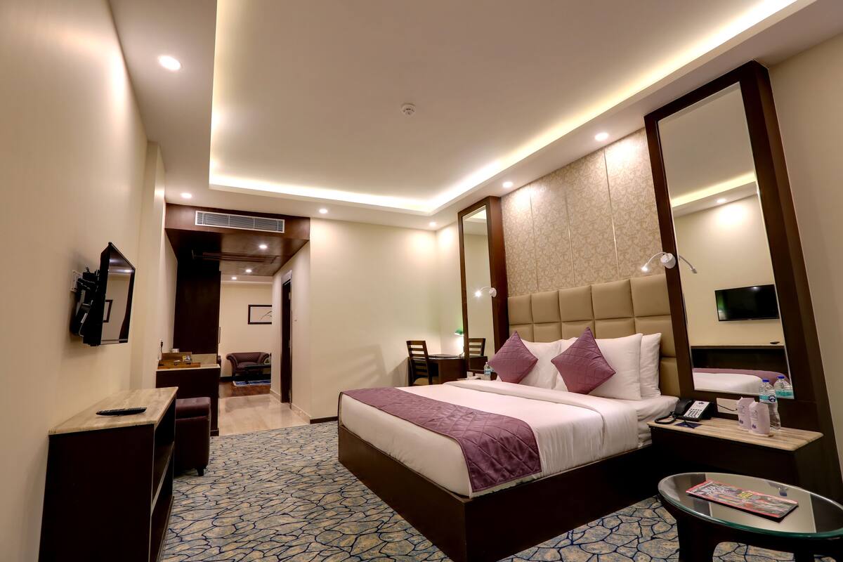 A modern hotel room with a large bed, bedside tables, a glass coffee table, and a TV.