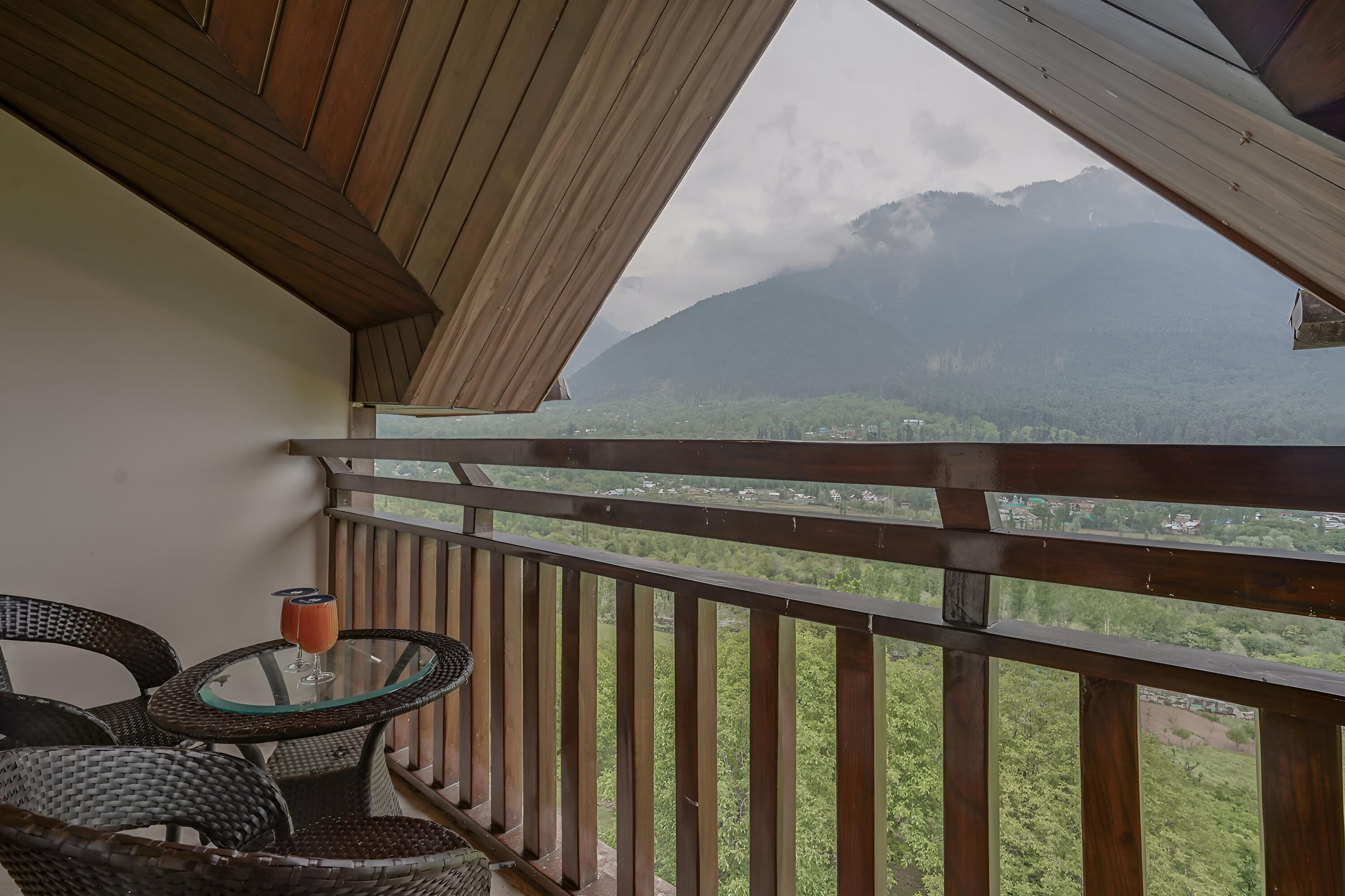 A balcony with wicker chairs and a glass table, overlooking a mountainous landscape.