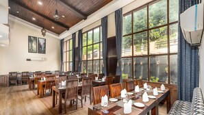 A dining area with wooden tables and chairs, large windows with curtains, and a ceiling with wooden beams and recessed lighting. - The Chinar Resort & Spa, Pahalgam (Anantnag)