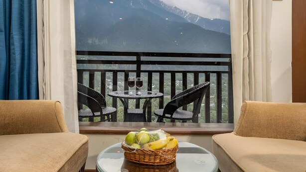A balcony with a wicker basket of fruit, two chairs, and a table with wine glasses. - The Chinar Resort & Spa, Pahalgam (Anantnag)