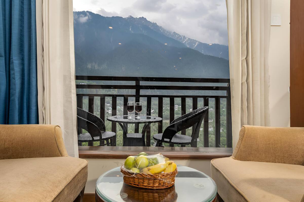 A balcony with a wicker basket of fruit, two chairs, and a table with wine glasses.