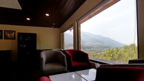 A room with a large window offering a mountain view, a small table, and two chairs. - The Chinar Resort & Spa, Pahalgam (Anantnag)