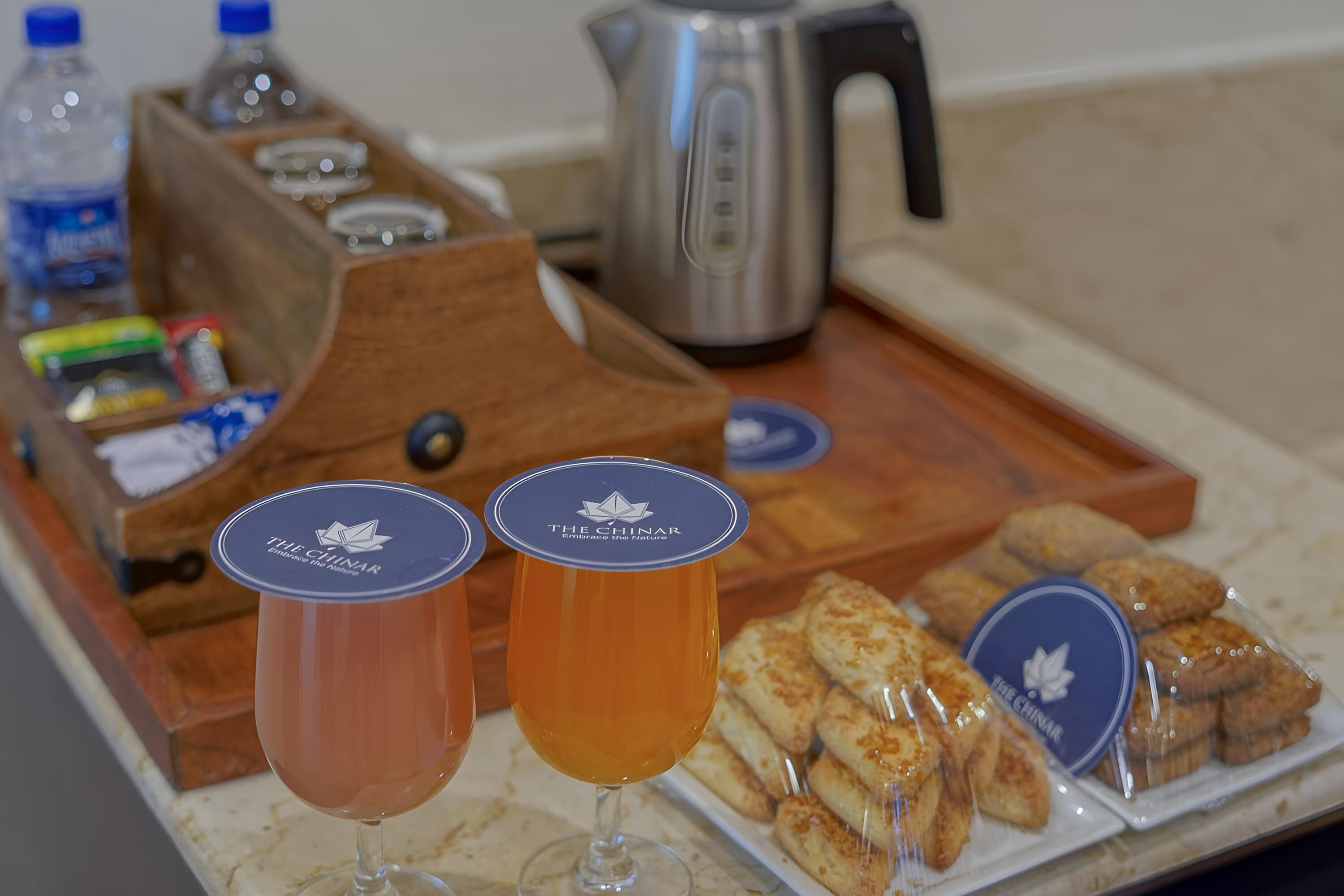 A tray with two glasses of tea, a kettle, and packaged snacks.