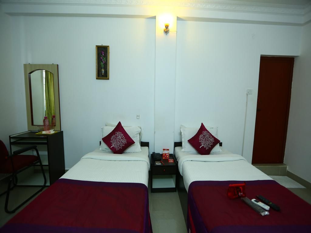 A hotel room with two beds, a desk, a chair, a mirror, and a door.
